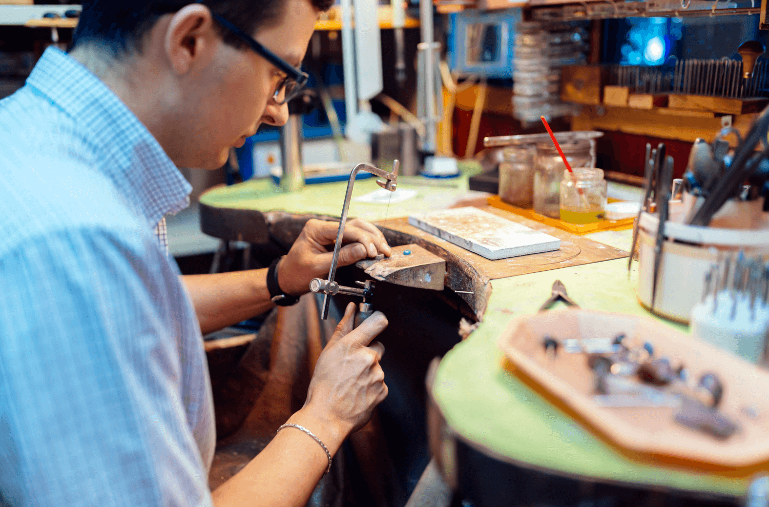 Man in his workshop, focused on crafting a special piece of jewelry, surrounded by various tools on his work desk Man in his workshop, focused on crafting a special piece of jewelry, surrounded by various tools on his work desk