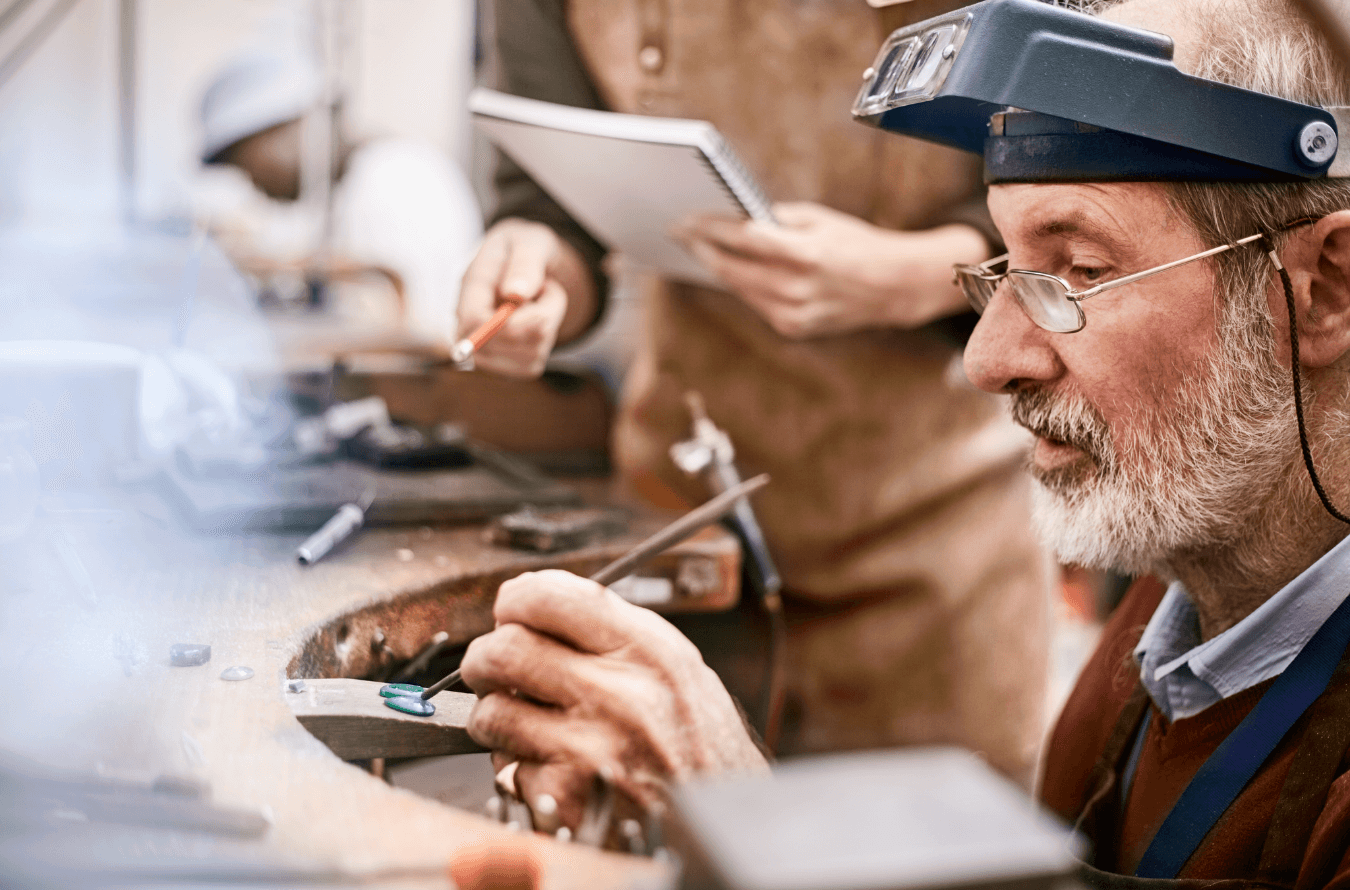 Man in his workshop, focused on crafting a special piece of jewelry, surrounded by various tools on his work desk. Man in his workshop, focused on crafting a special piece of jewelry, surrounded by various tools on his work desk.
